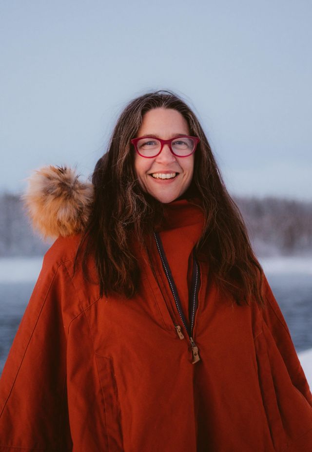 tracey williams woman stands outside near frozen lake with red parka